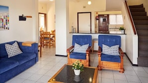 Una sala de estar con un sofá, dos sillones, una mesa de centro y una cocina al fondo.