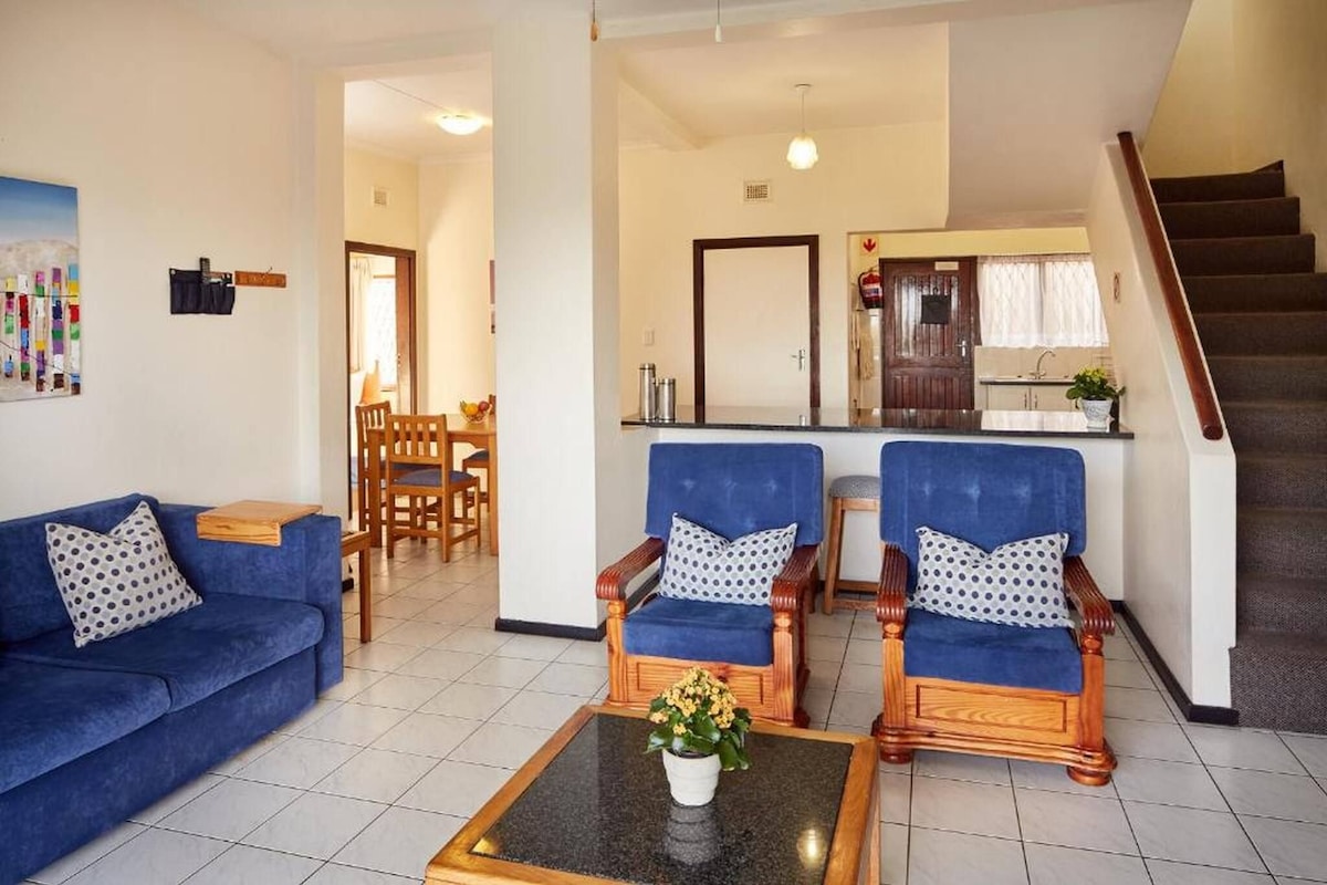 A living room with a sofa, two armchairs, a coffee table, and a kitchen area in the background.