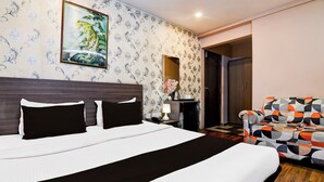 Une chambre d’hôtel avec un grand lit, un mur orné de motifs, un tableau représentant un tigre, un miroir, un bureau avec une lampe et une chaise colorée.