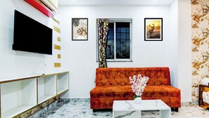 Un salon comprenant un canapé, un téléviseur à écran plat, une fenêtre avec des rideaux et un mur orné de tableaux.