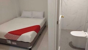 Un llit individual amb llençol vermell, almoina blanca i capçal de llit blanc en una habitació amb terra de marbre i vàter blanc.