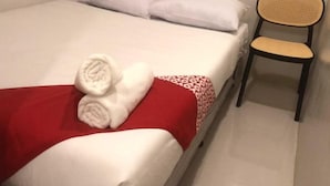 Un llit amb roba de llit blanca, un llençol vermell i tovalloles arremolinades. Hi ha una cadira amb respatller trenat.