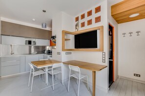 A modern kitchen with a dining area, a large flat-screen TV mounted on the wall, and a wooden table with chairs. - Beautiful 1-BR on Île de la Cité (Paris)