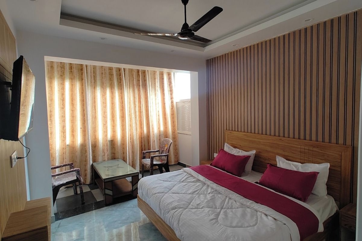 Une chambre d’hôtel équipée d’un lit, d’un bureau, d’une chaise, d’un ventilateur de plafond et d’une fenêtre avec des rideaux.