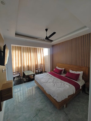 Une chambre d’hôtel équipée d’un lit, d’un bureau, d’une chaise, d’un ventilateur de plafond et d’une fenêtre avec des rideaux.
