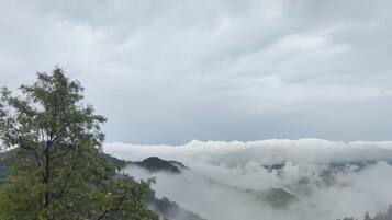 A mountainous landscape with a house nestled among trees, surrounded by clouds.