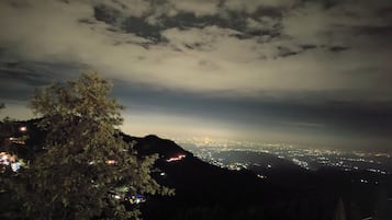 Vista noturna de uma paisagem urbana com uma montanha ao primeiro plano e um céu nublado.