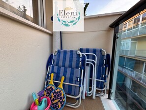 Ein Balkon mit Blick auf ein Gebäude, ein Schild mit dem Namen 'Eleni Estepona' und eine Reihe blauer und gelber Strandstühle.