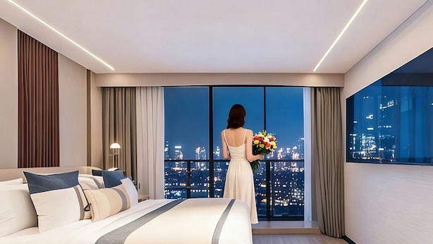 A modern hotel room with a large bed, a city view, and a person holding a bouquet of flowers. - Yunli Cloudtop Hotel (Guangzhou)