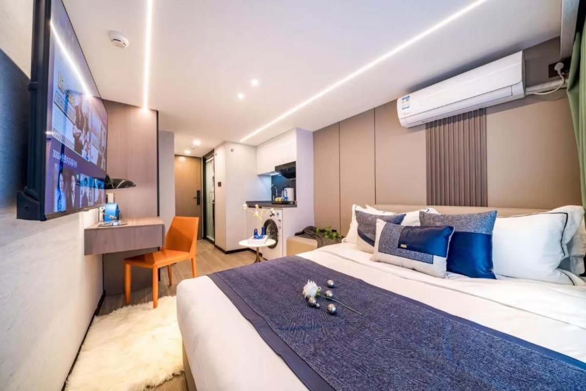 Una camera d'albergo moderna con un letto, una scrivania, una sedia, una TV e un condizionatore d'aria.