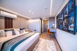 Una moderna camera d'albergo con un letto, una scrivania e una sedia.  C'è un quadro appeso al muro e un condizionatore d'aria sopra il letto.