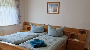 Cama doble con cabecera de madera, dos almohadas, mesita de noche con cajón y un cuadro en la pared.