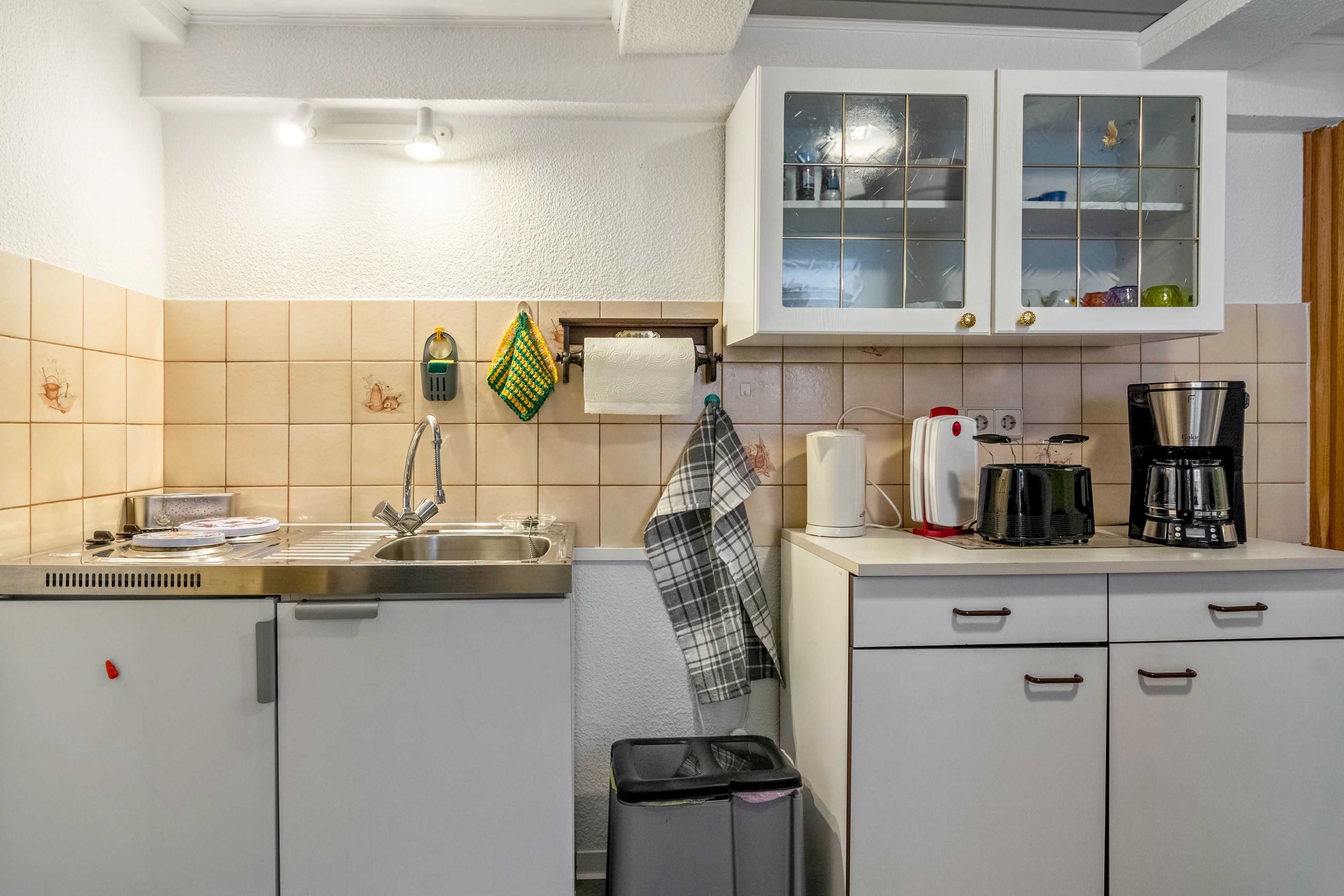 Eine Küche mit weißen Schränken, einer Edelstahl-Spüle, einer Kaffeemaschine und einem Wasserkocher.