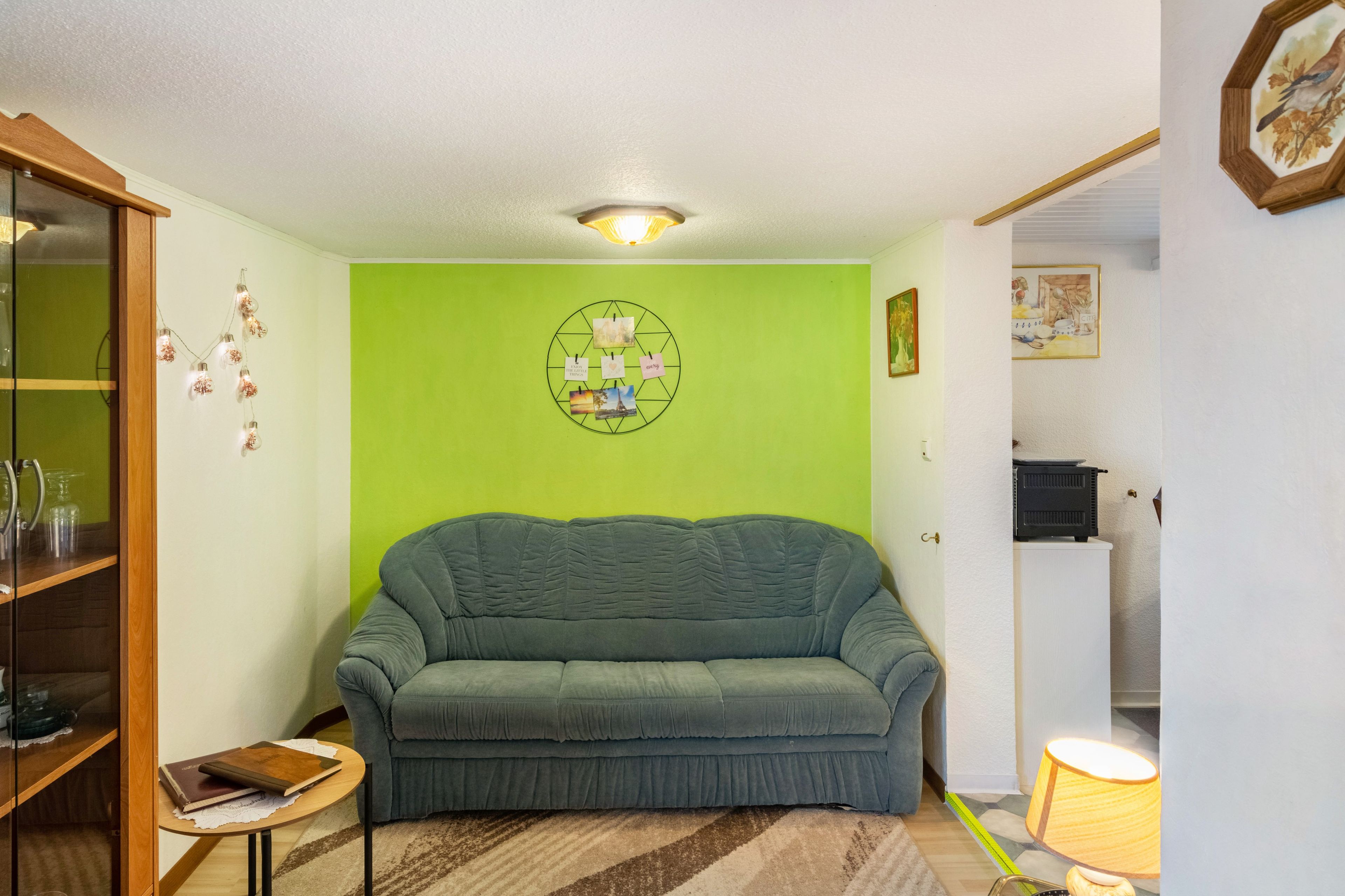 A living room with a green wall, a sofa, a small table with books, and a decorative light fixture.