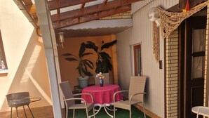 Un área de patio techada con una mesa, sillas, una parrilla y una planta en maceta.