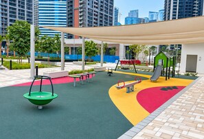 An outdoor play area with a swing, slide, and climbing structure. - HAVN - Cozy Studio in Peninsula 3, Business Bay (Dubai)