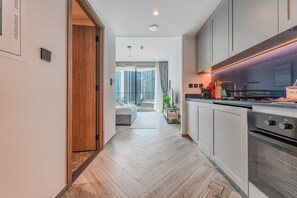 A modern kitchen with white cabinets, a stainless steel oven, and a dining area with a table and chairs. - HAVN - Cozy Studio in Peninsula 3, Business Bay (Dubai)