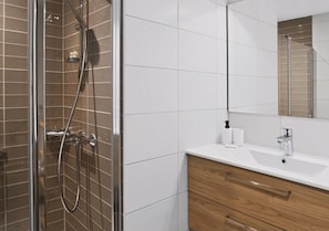 Un baño moderno con ducha envuelta en vidrio, un lavamanos blanco y un mueble de tocador de madera.