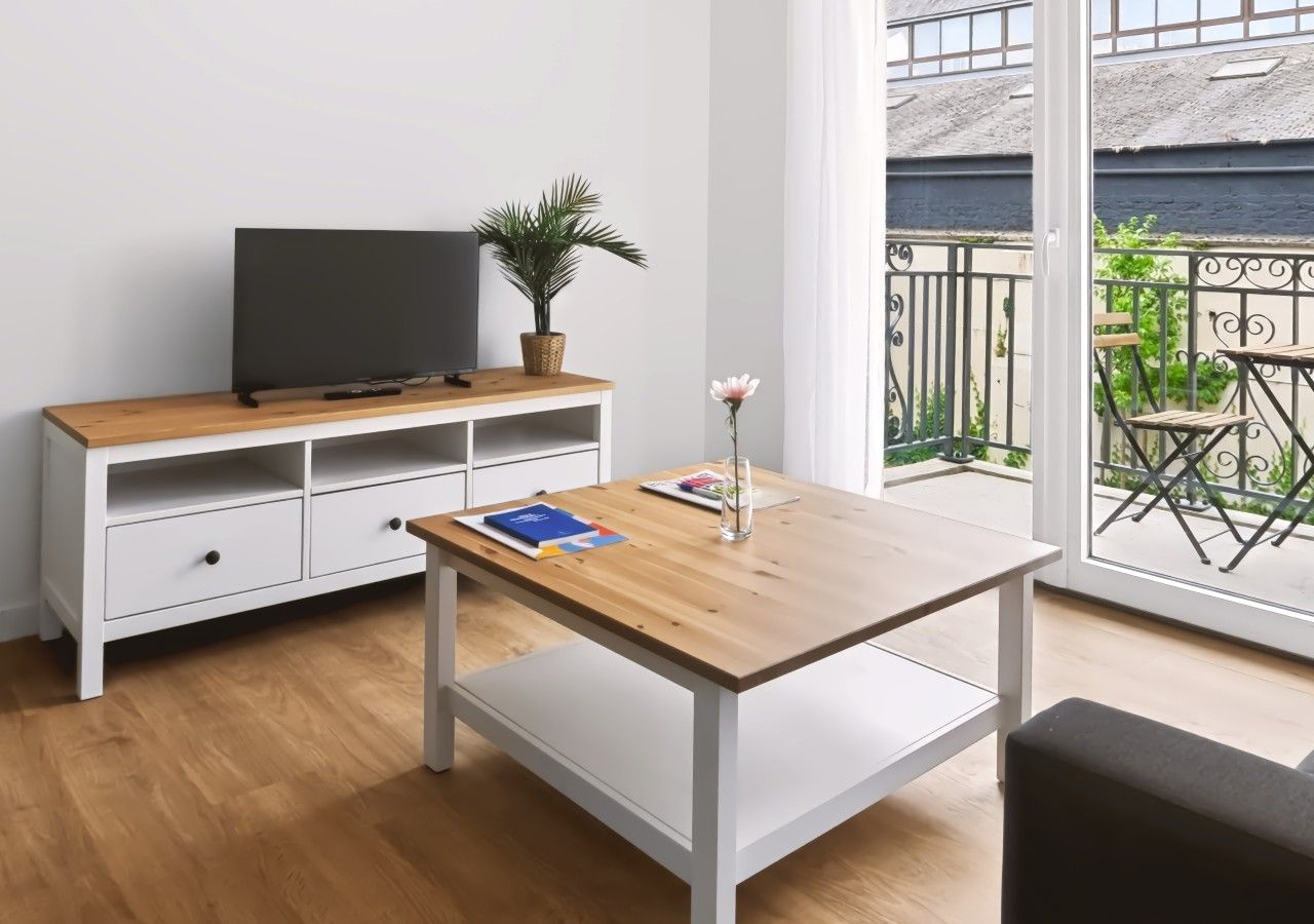 Una habitación con una mesa de madera, un mueble blanco para televisor y un balcón con vistas.