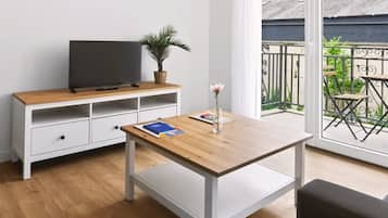 Una habitación con una mesa de madera, un mueble blanco para televisor y un balcón con vistas.