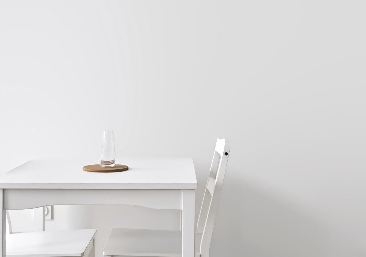 Una mesa blanca con un vaso y un posavasos, y una silla blanca.