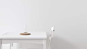 Una mesa blanca con un vaso y un posavasos, y una silla blanca.