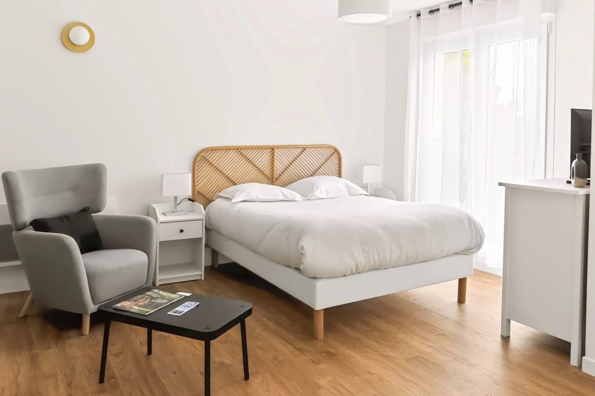 Un dormitorio moderno con cama, mesitas de noche, una silla, una pequeña mesa y una lámpara.