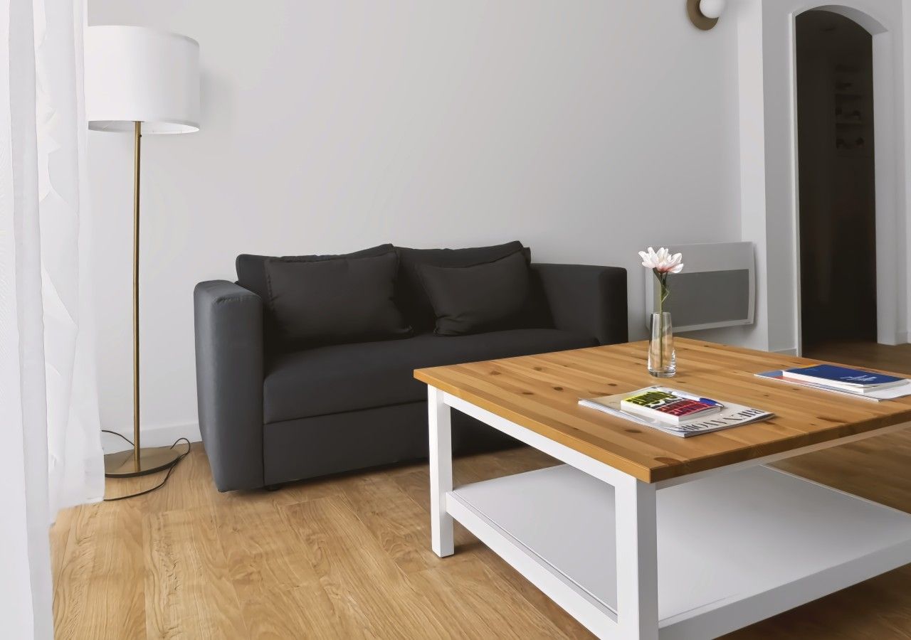 Una sala moderna con un sofá gris, una mesa de centro de madera y una lámpara de pie.