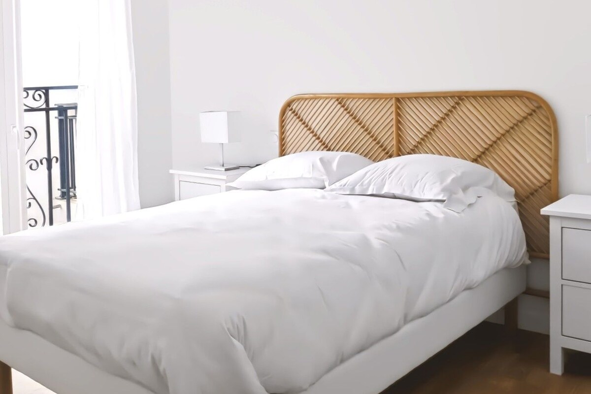 Una cama con cabecera de mimbre, ropa de cama blanca y una mesita de noche con lámpara.