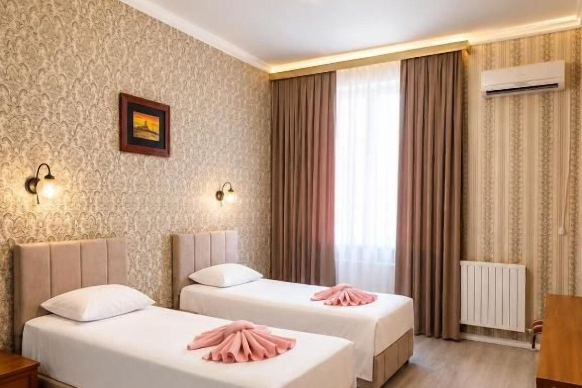 A hotel room with two beds, a wooden floor, a radiator, and a picture on the wall.
