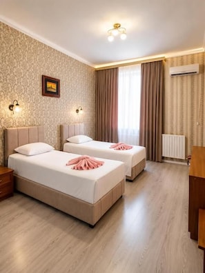 A hotel room with two beds, a wooden floor, a radiator, and a picture on the wall. - HAYAT inn KHIVA (Khiva)
