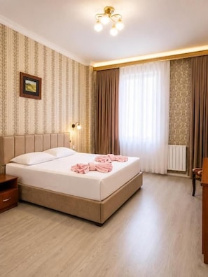 A hotel room with a large bed, a bedside table, a nightstand, a lamp, and a window with curtains. - HAYAT inn KHIVA (Khiva)