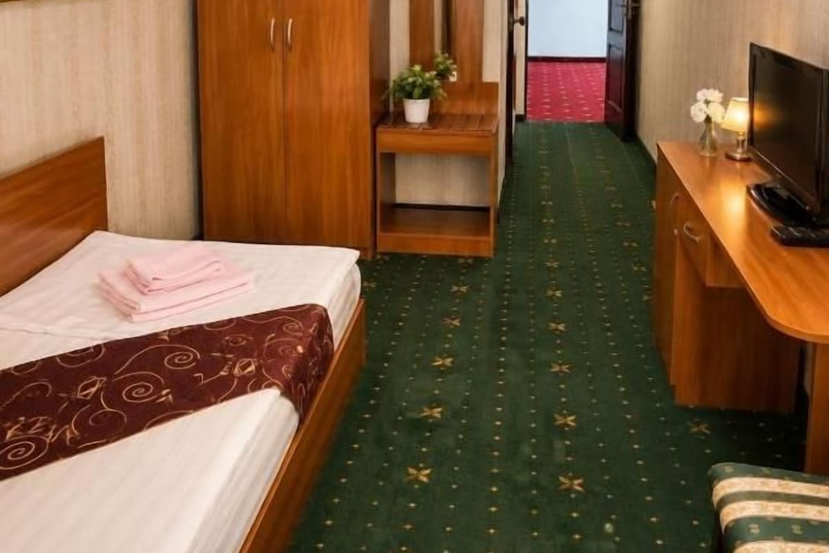 A hotel room with a bed, a desk, a wardrobe, and a view of the city.