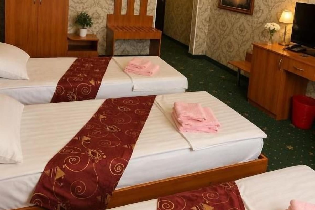 A hotel room with three beds, a wooden wardrobe, a desk, a chair, and a television.