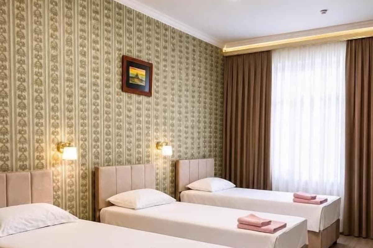 A hotel room with three beds, a wooden floor, a patterned wallpaper, and a picture on the wall.