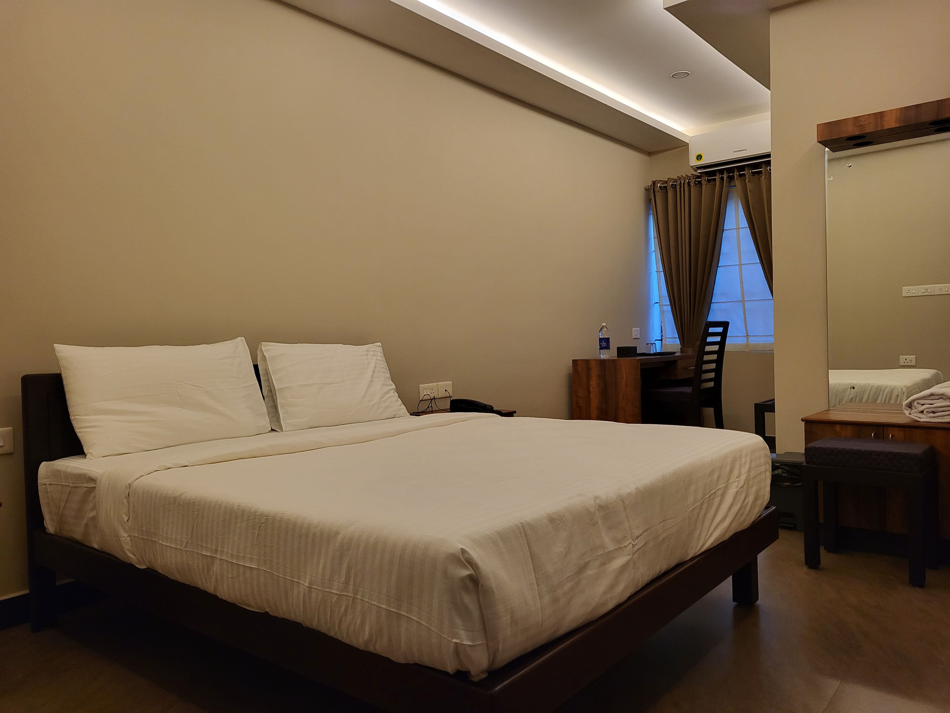 Ein Hotelzimmer mit einem großen Bett, einem Schreibtisch, einem Stuhl und einem Vorhangfenster.