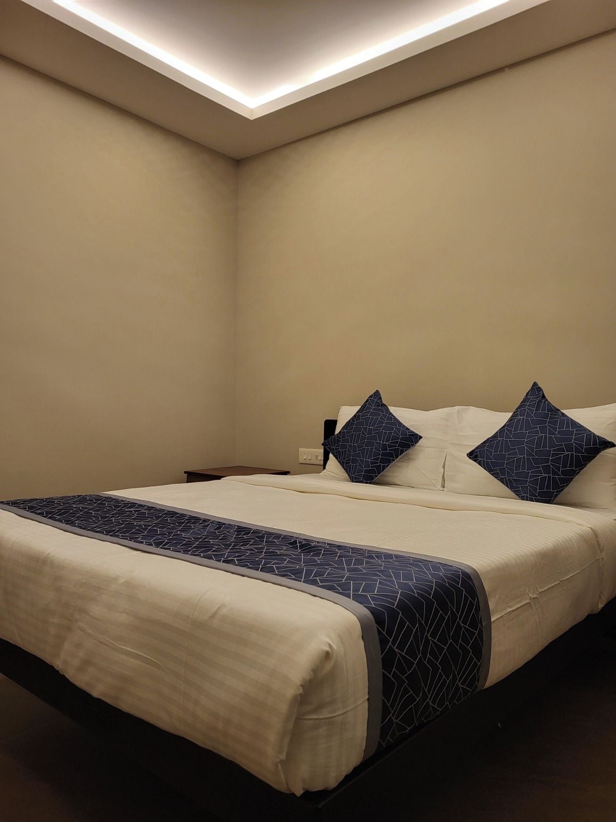 Una habitación de hotel con cama, mesita de noche y una lámpara en el techo.