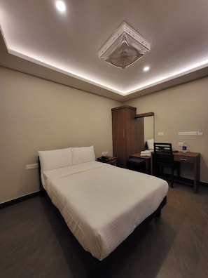 Habitación de hotel con una cama grande, un escritorio, una silla, un armario y una lámpara en el techo.
