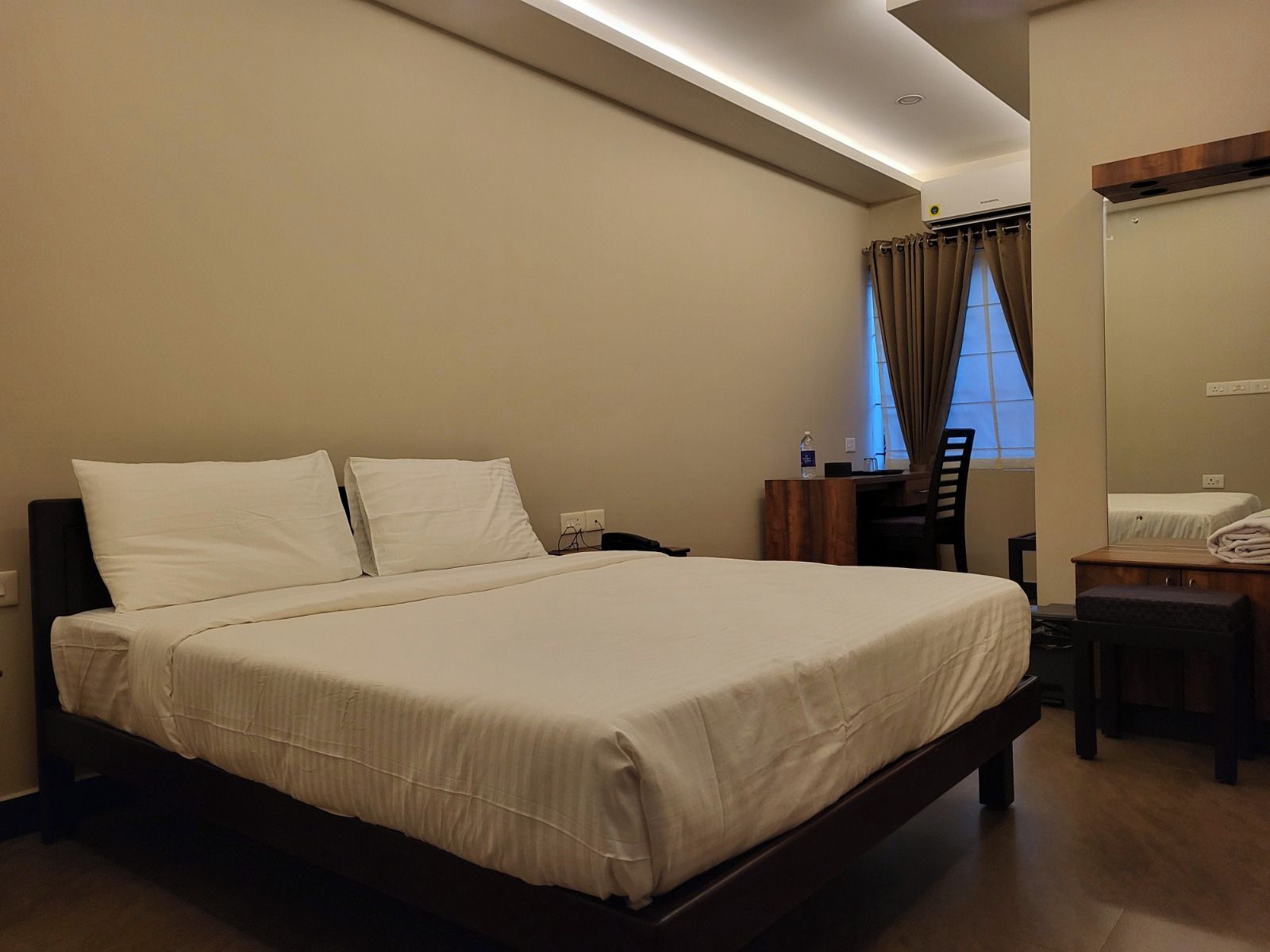 A hotel room with a large bed, a desk, a chair, and a window with curtains.