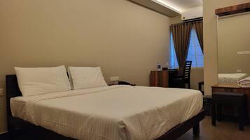 A hotel room with a large bed, a desk, a chair, and a window with curtains.