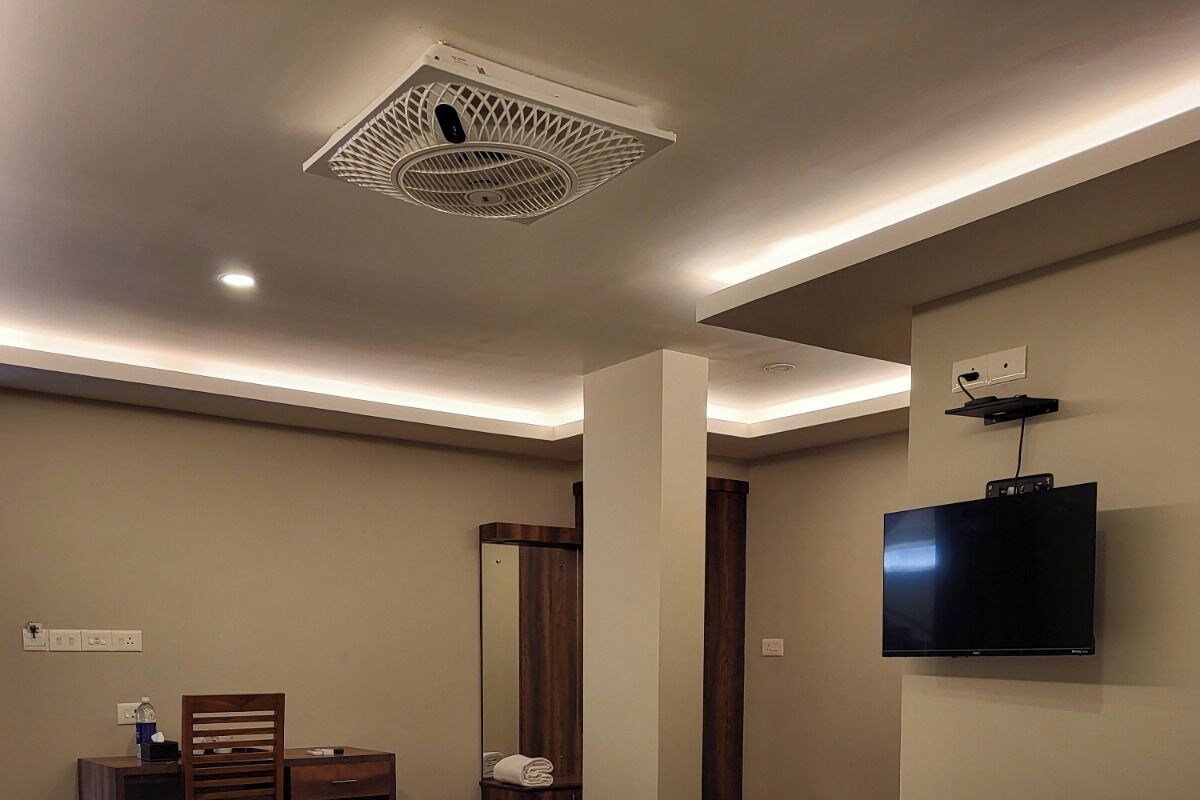 A hotel room with two beds, a desk, a chair, a television, and a ceiling fan.