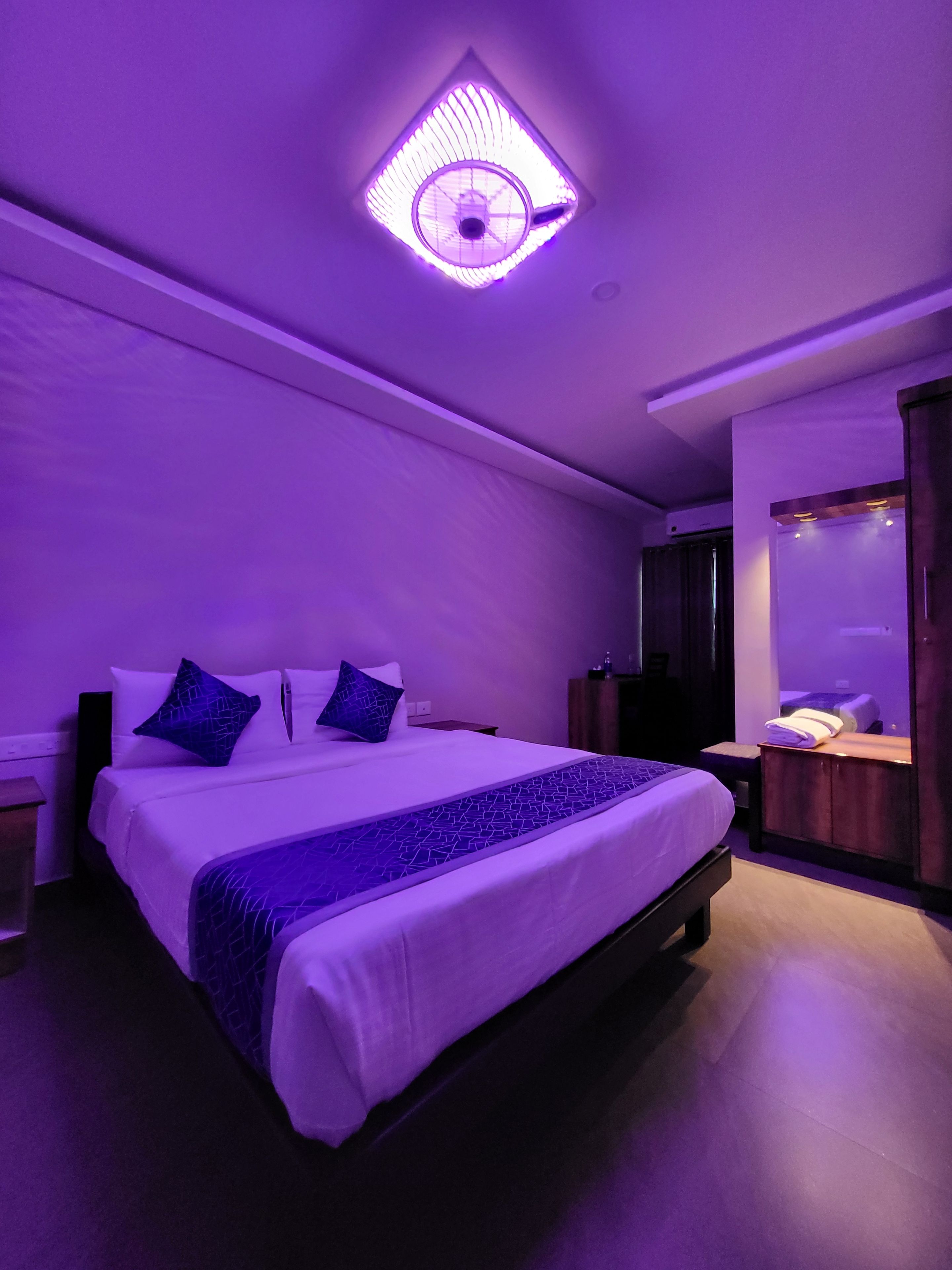 A hotel room with a large bed, a bedside table, a mirror, and a ceiling light fixture.