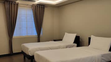 A hotel room with two beds, a window with curtains, a ceiling vent, and a wall-mounted air conditioning unit.