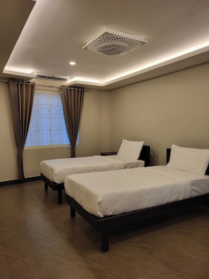 Habitación de hotel con dos camas, una ventana con cortinas, un respiradero en el techo y un aire acondicionado instalado en la pared.