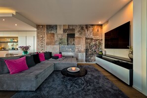 Una sala de estar moderna con un sofá modular, un televisor de pantalla plana y una pared decorativa con una mezcla de texturas y patrones.
