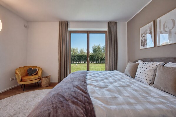 Ein Schlafzimmer mit einem großen Bett, einem Sessel und Blick auf eine grüne Landschaft durch ein Fenster.