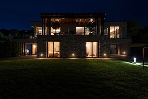 Ein modernes, zweistöckiges Haus mit Natursteinfassade, großen Glasüren und einem gut beleuchteten Innenraum.