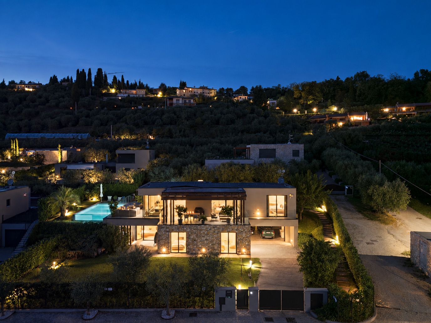 A modern house with a swimming pool, surrounded by lush greenery and a hilly landscape.
