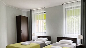 Quarto de hotel com duas camas, um guarda-roupa e grandes janelas com cortinas.
