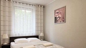 Quarto de hotel com cama, duas luminárias de cabeceira, janela com cortinas e um quadro na parede.